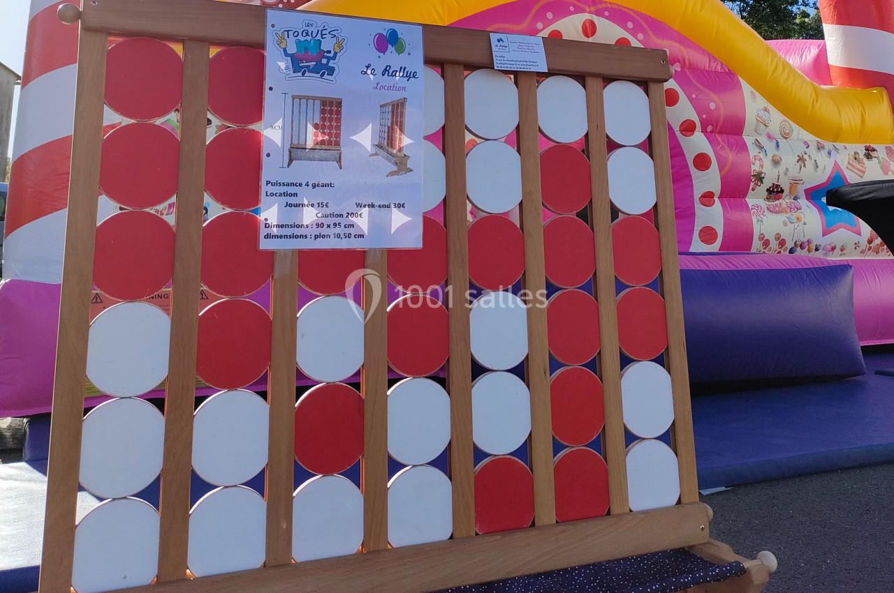 Jeu de puissance 4 géant en bois avec des pions rouges et blancs, installé devant une structure gonflable colorée.