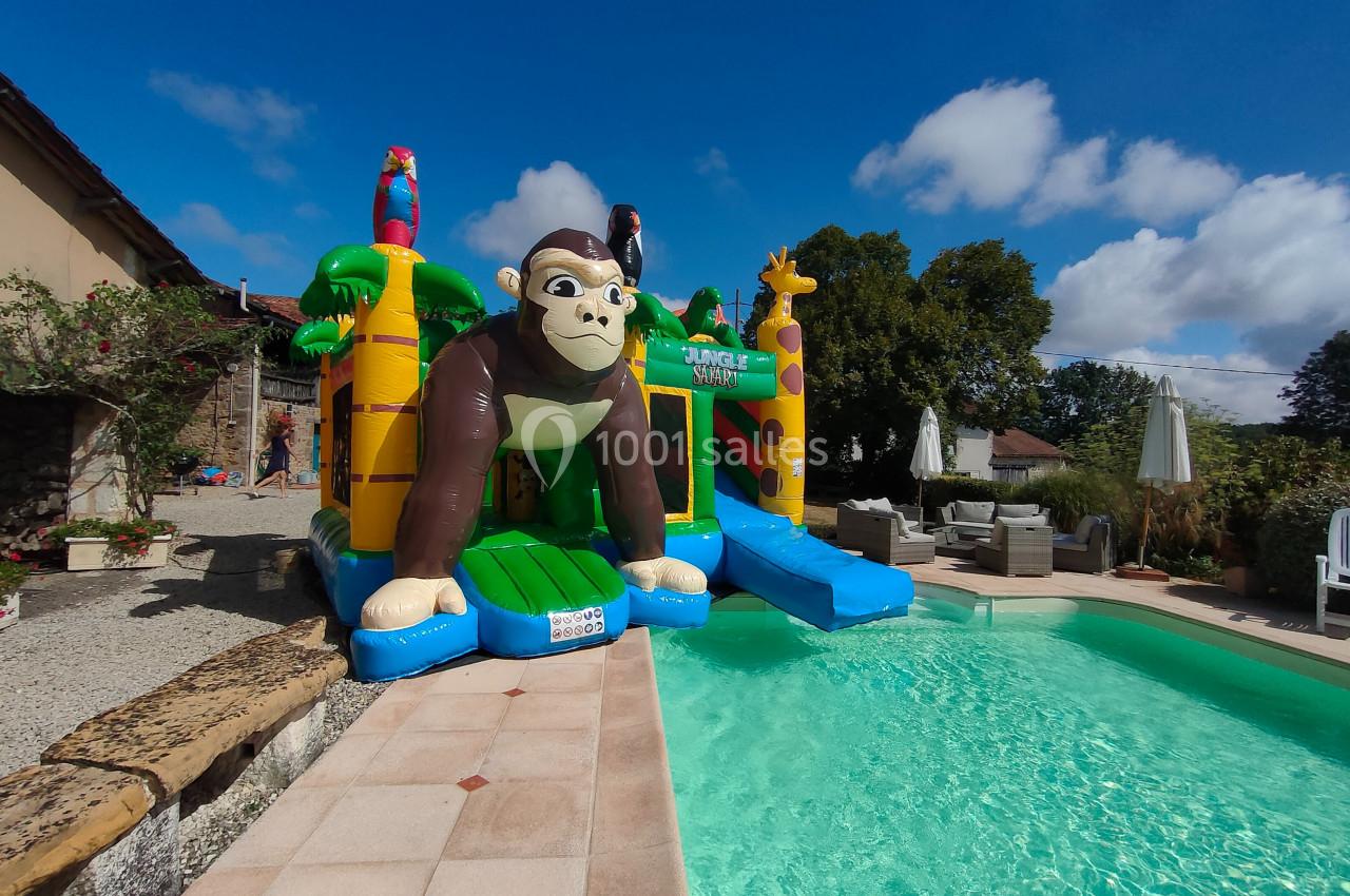 Structure gonflable avec un gorille et des animaux colorés, installée près d'une piscine dans un jardin ensoleillé.