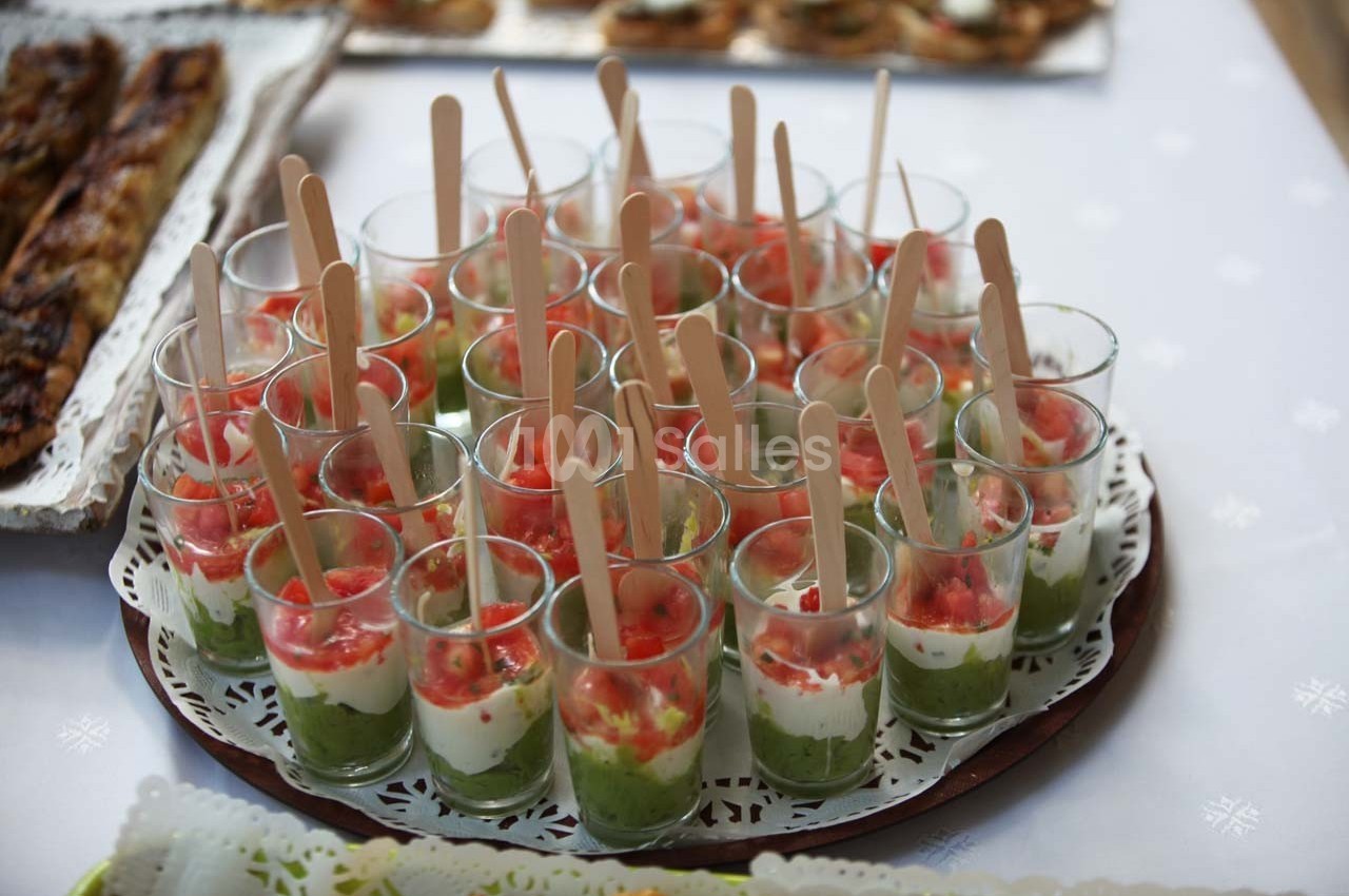 Verrines apéritives avec couches de guacamole, crème et tomates, servies avec des cuillères en bois sur un plateau.