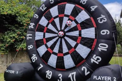 Un jeu de puissance 4 géant en bois placé sur une pelouse, à côté d'une girouette rouge sous des arbres.