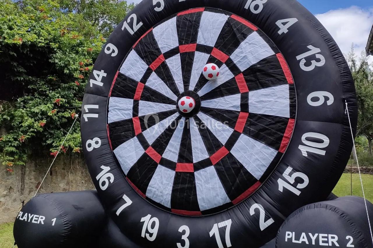 Cible géante gonflable noire avec des balles à scratch, installée dans un jardin verdoyant.