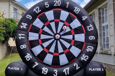 Un jeu de puissance 4 géant en bois placé sur une pelouse, à côté d'une girouette rouge sous des arbres.