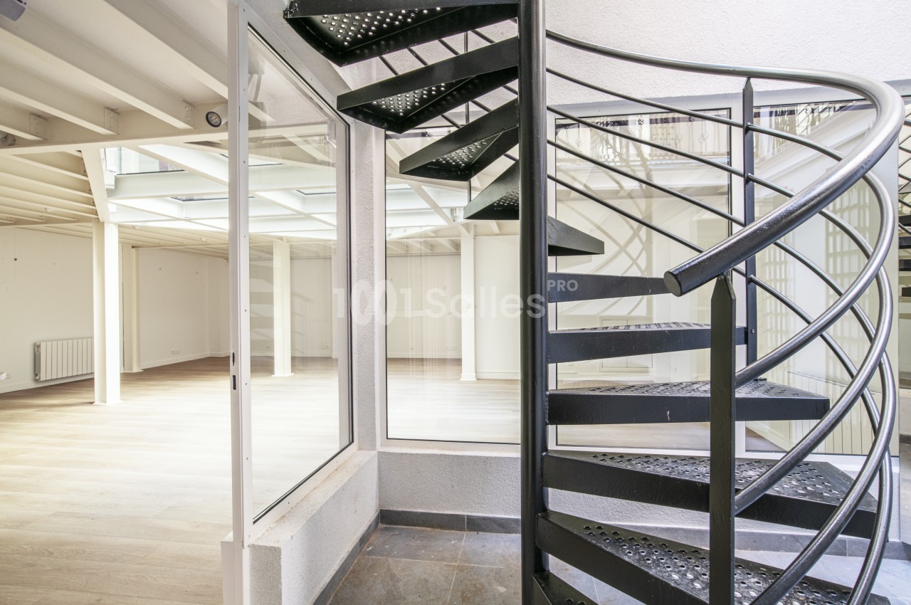 Escalier en colimaçon en métal noir dans un espace intérieur lumineux avec parquet et murs blancs.