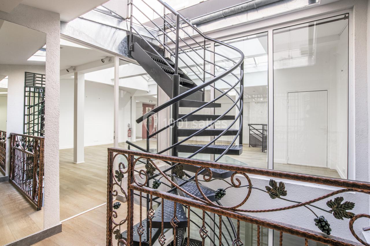 Escalier en colimaçon métallique dans un espace intérieur lumineux avec parquet et balustrades décoratives.