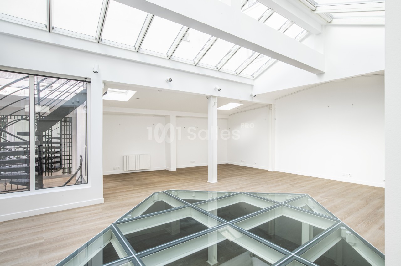 Espace intérieur lumineux avec verrière, parquet clair et sol vitré, donnant sur un escalier en colimaçon.