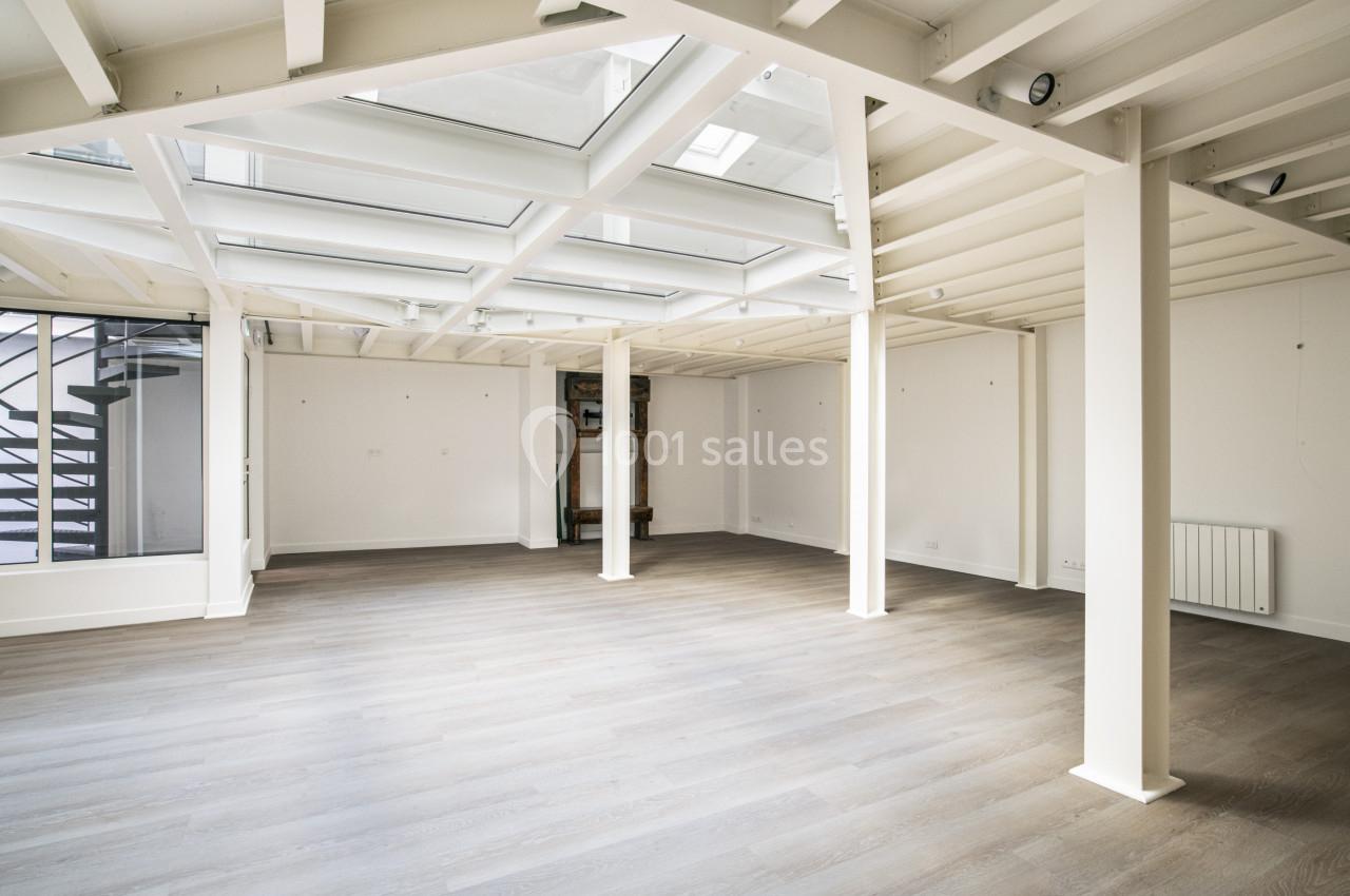 Grand espace intérieur lumineux avec parquet clair, poutres blanches apparentes et puits de lumière au plafond.
