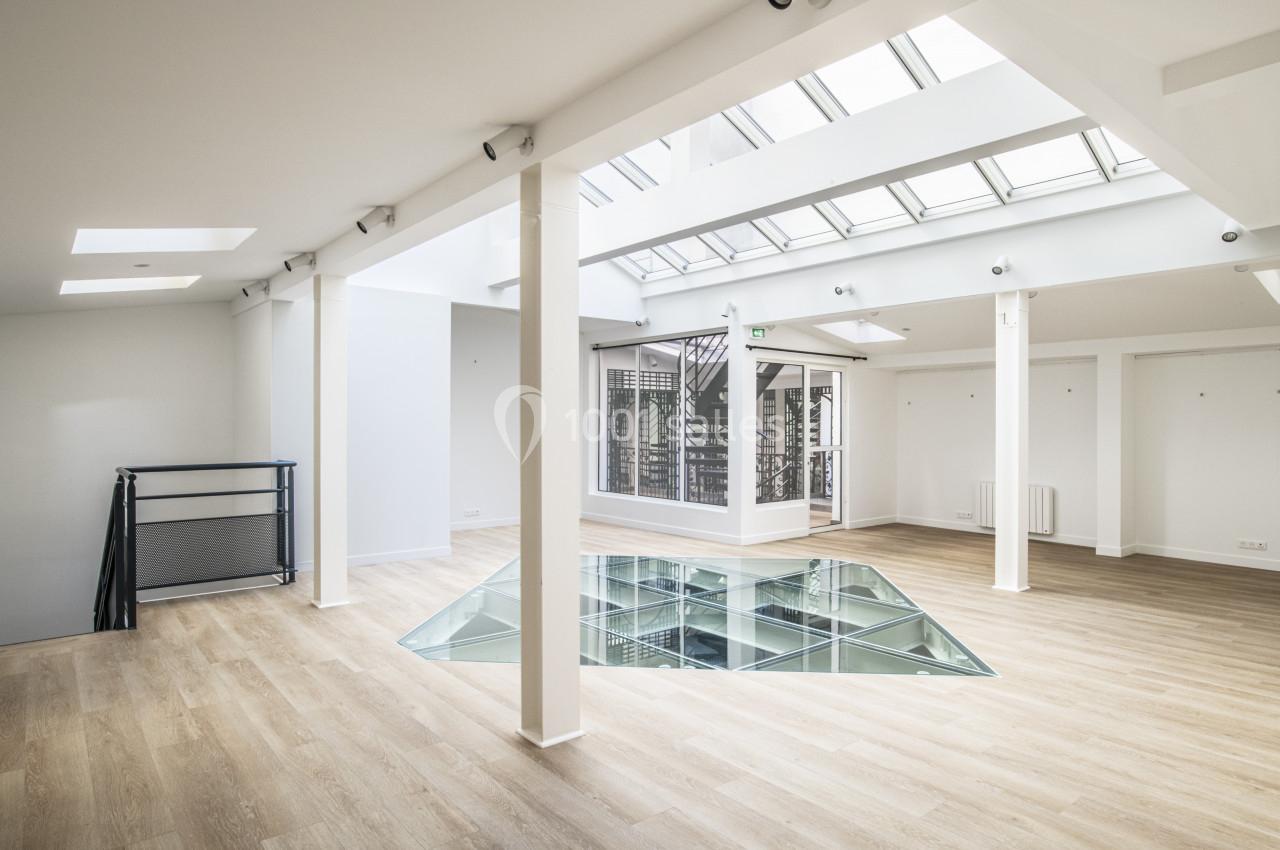 Espace intérieur lumineux avec parquet clair, verrière au plafond et ouverture vitrée au sol.