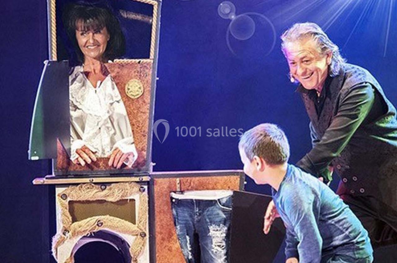 Un magicien réalise un tour avec une femme dans une boîte et un enfant observant la scène sur scène.