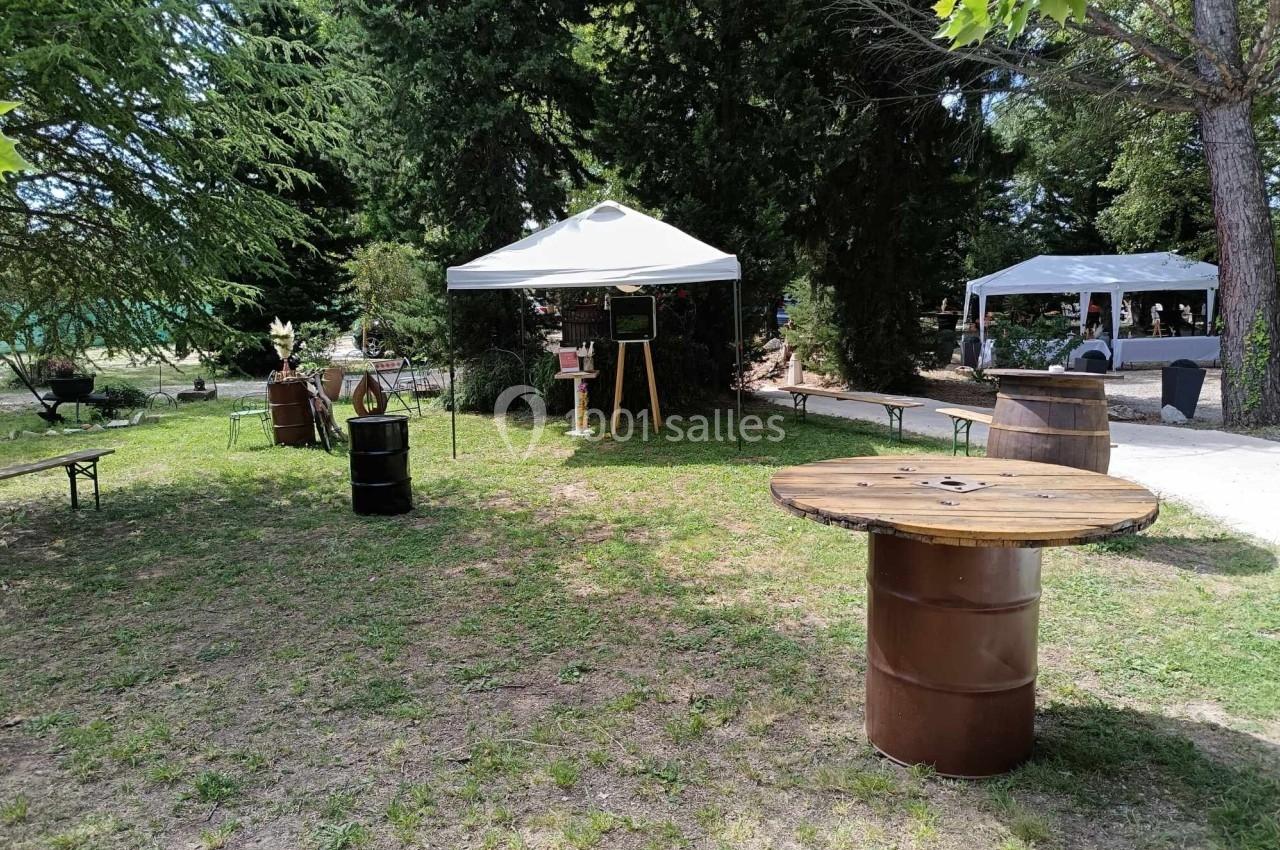 Espace extérieur avec tonnelles blanches, tables en tonneaux et végétation environnante.