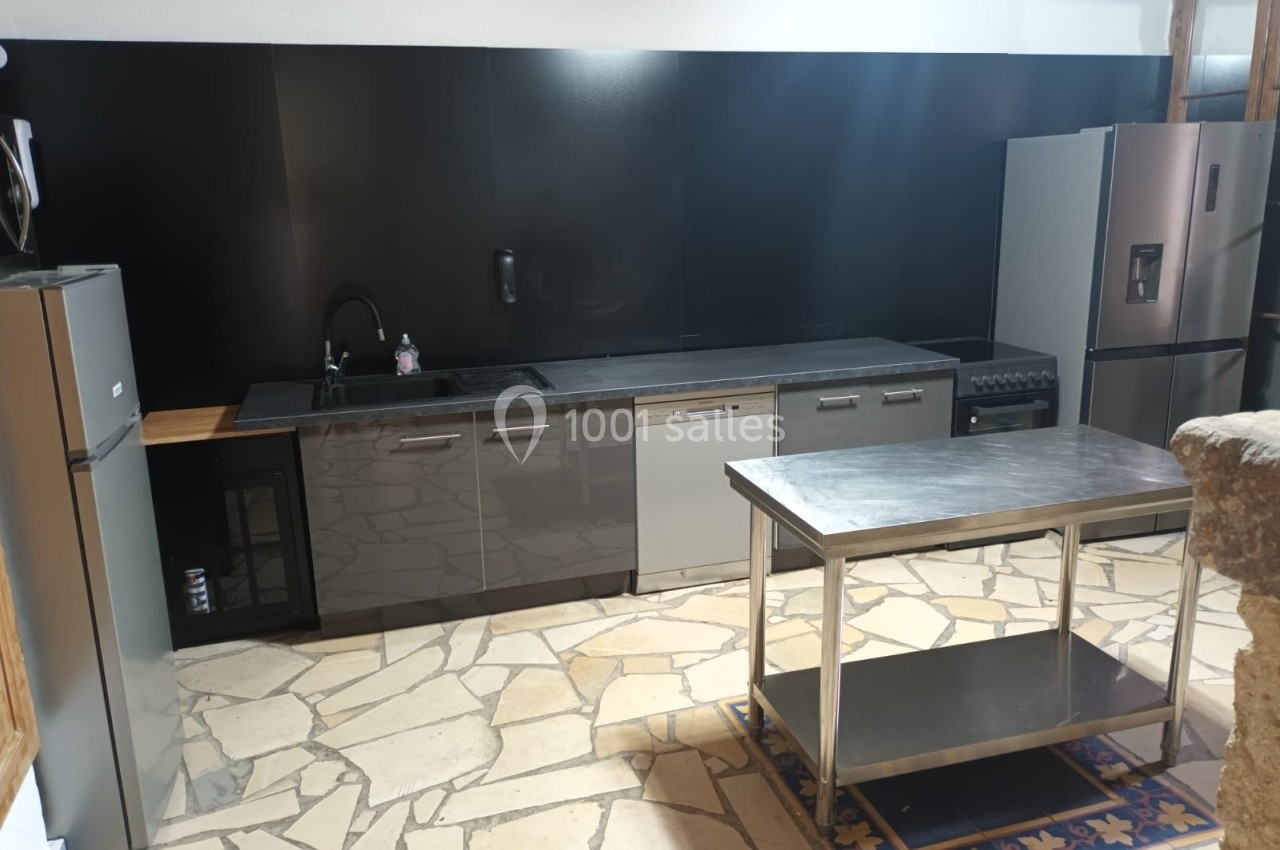 Cuisine moderne avec meubles gris, plan de travail noir, électroménagers en acier inoxydable et îlot central en métal.