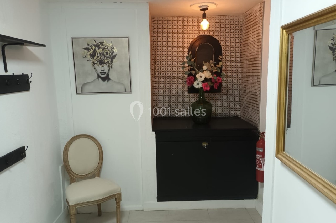 Coin décoratif avec chaise en bois, tableau, miroir, vase de fleurs et applique murale dans un espace lumineux.