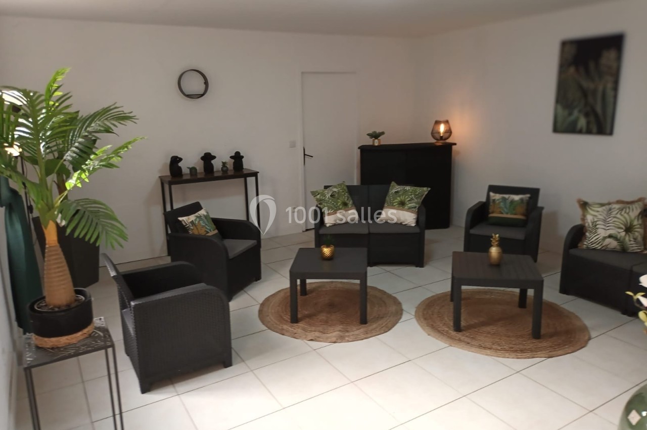 Salon moderne avec mobilier en rotin noir, coussins à motifs tropicaux, plantes décoratives et éclairage doux.