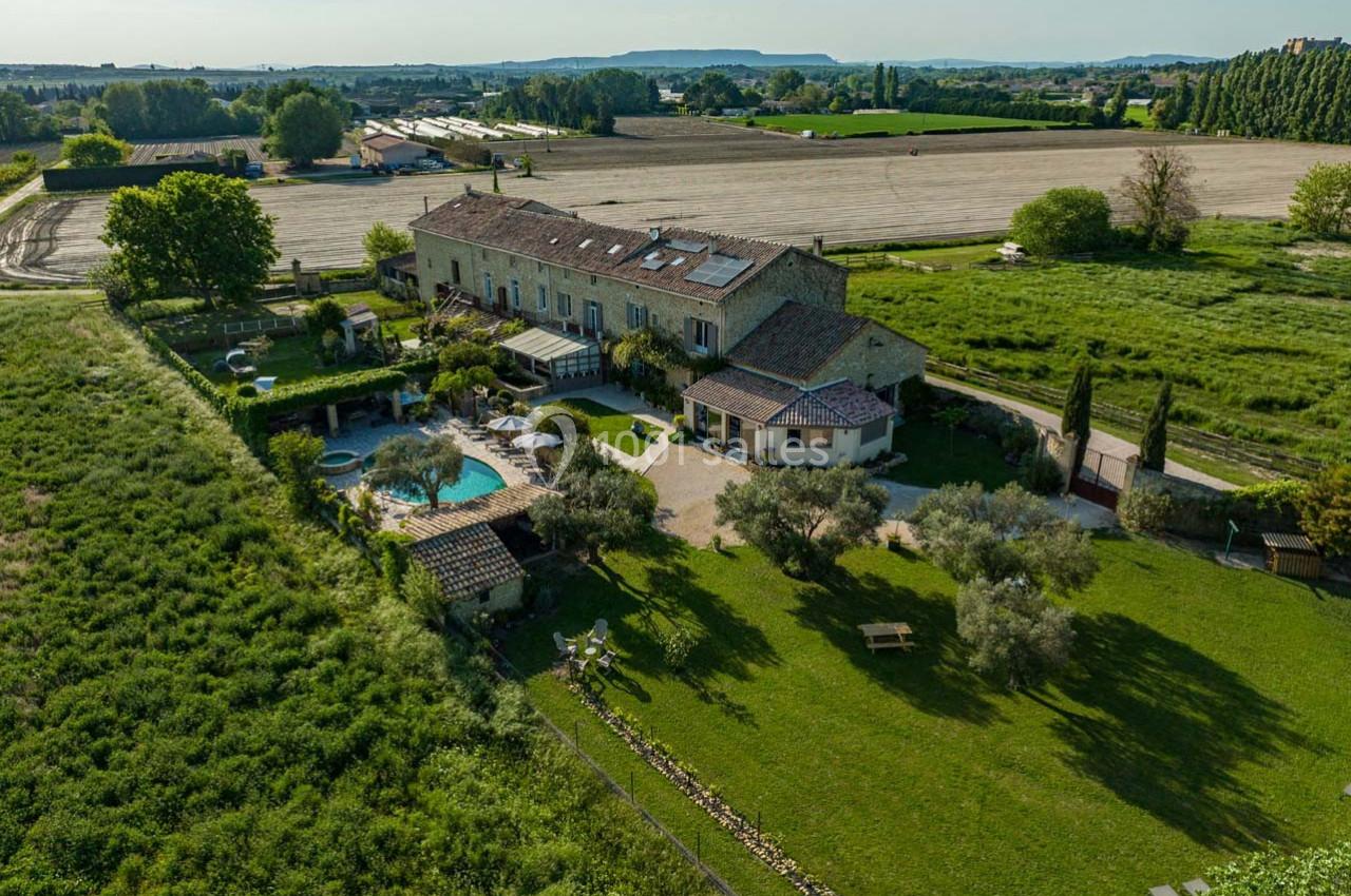 Vue aérienne d'une grande maison en pierre avec piscine, jardin aménagé et champs environnants sous un ciel dégagé.