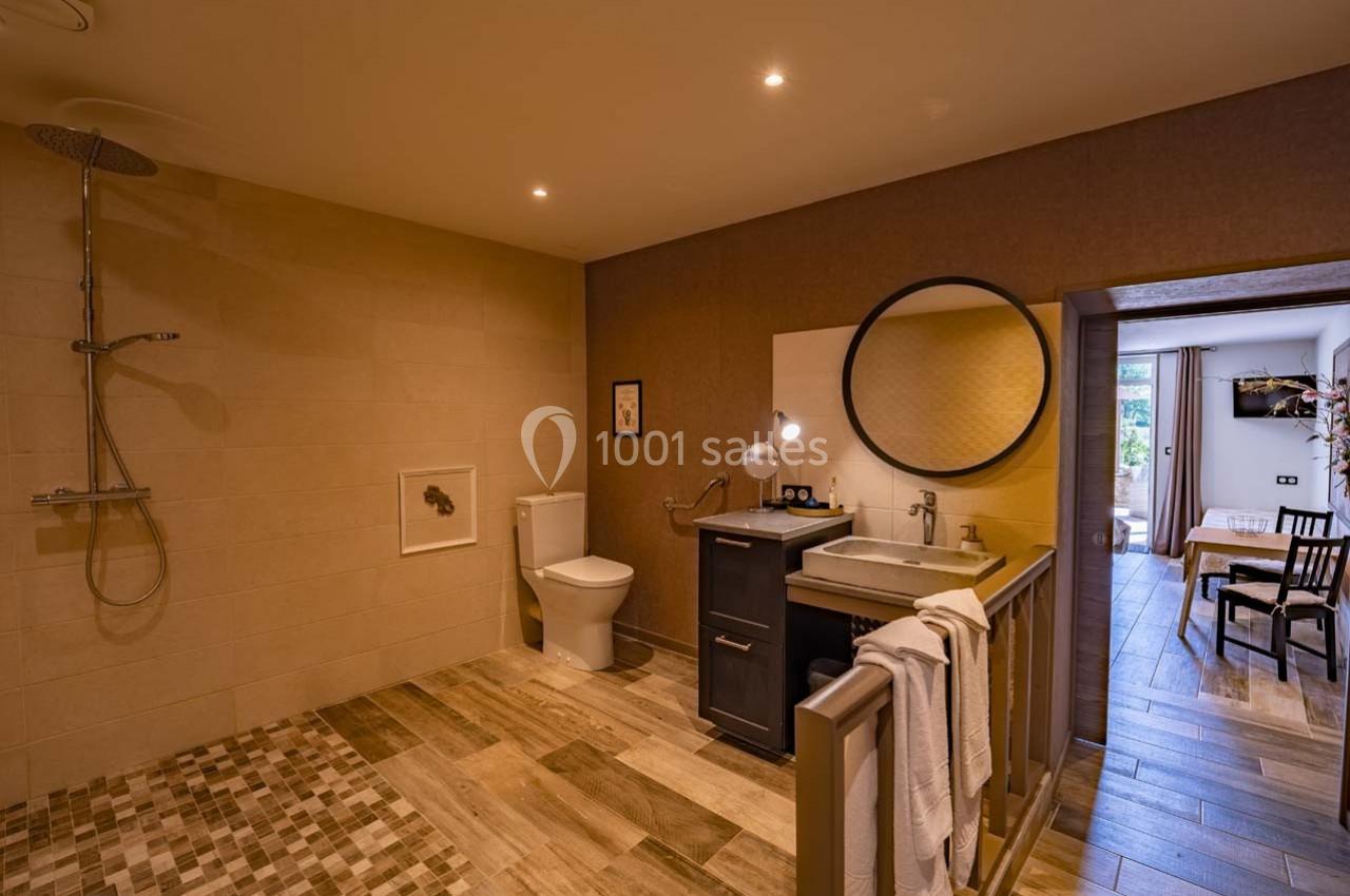 Salle de bain accessible avec douche à l'italienne, lavabo, miroir rond, toilettes et éclairage chaleureux.