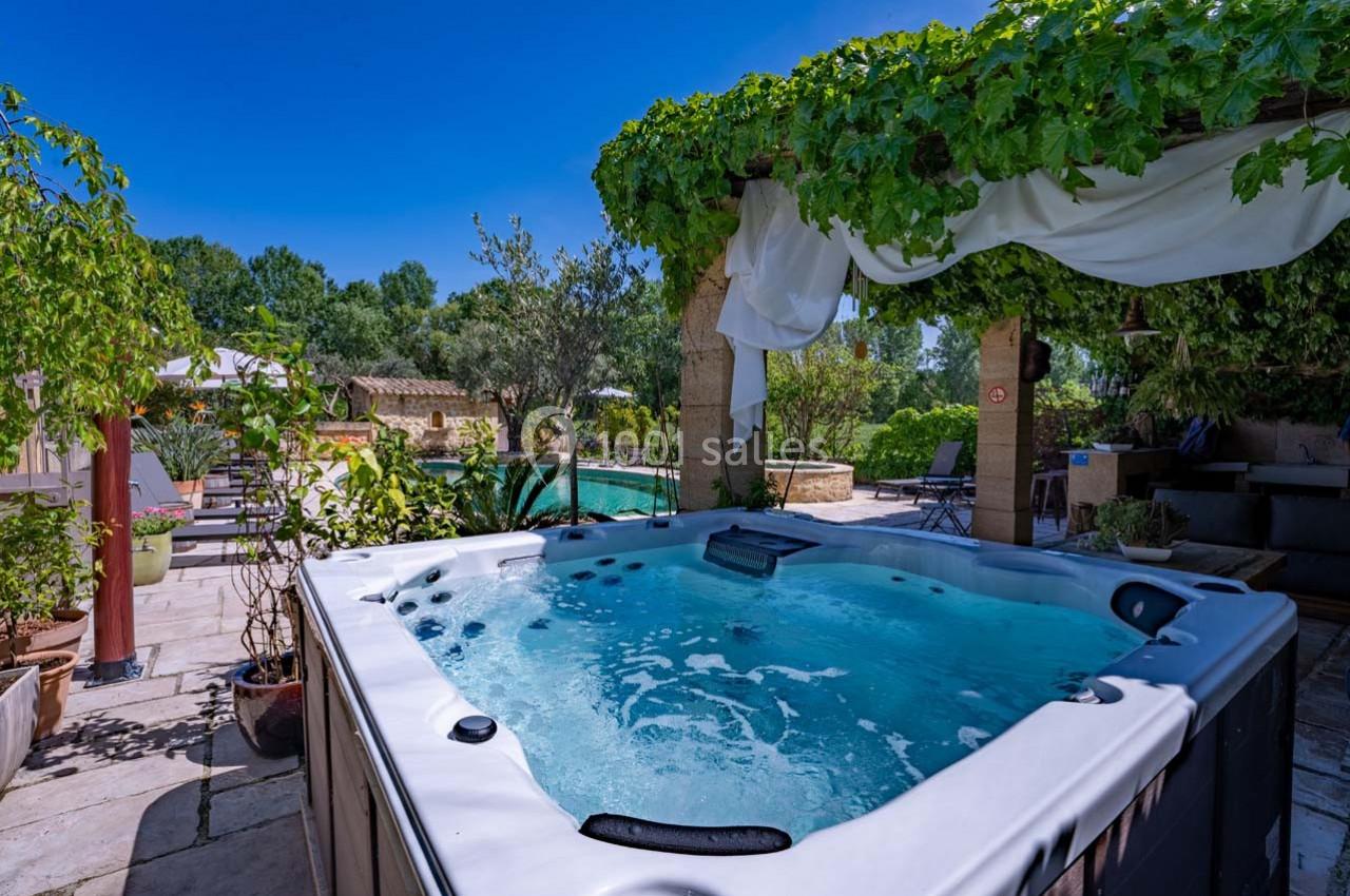Bain à remous extérieur sous une pergola végétalisée, avec vue sur une piscine entourée de verdure.