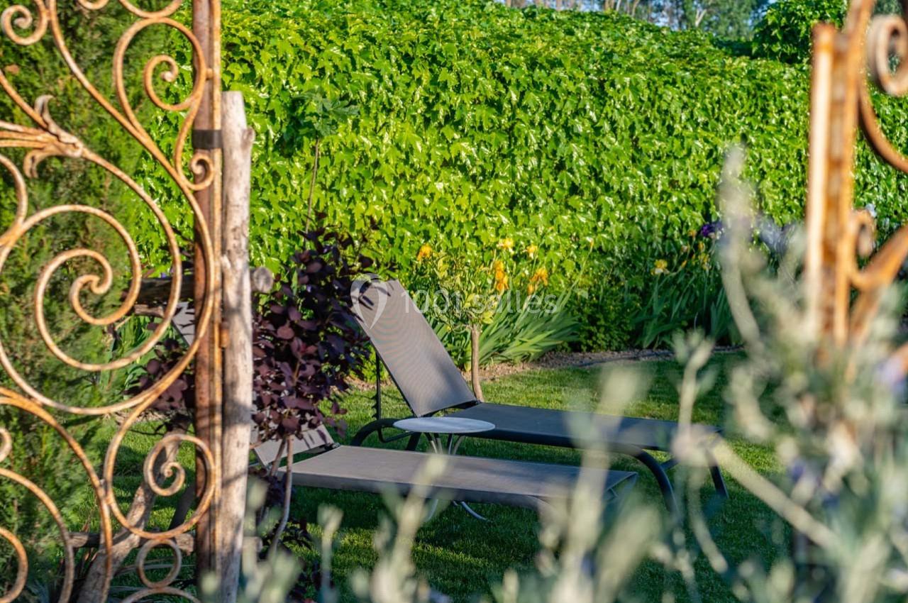 Deux transats installés dans un jardin verdoyant, entourés de végétation et d'une structure métallique décorative.