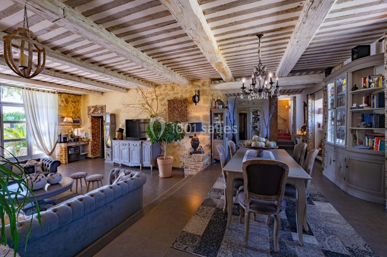 Salle à manger et salon dans une maison rustique avec poutres apparentes, murs en pierre et mobilier élégant.