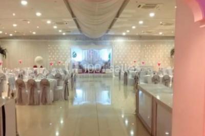 Salle de réception élégante avec tables dressées, chaises décorées et une estrade ornée de rideaux lumineux.