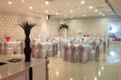 Salle de réception élégante avec tables dressées, chaises décorées et une estrade ornée de rideaux lumineux.