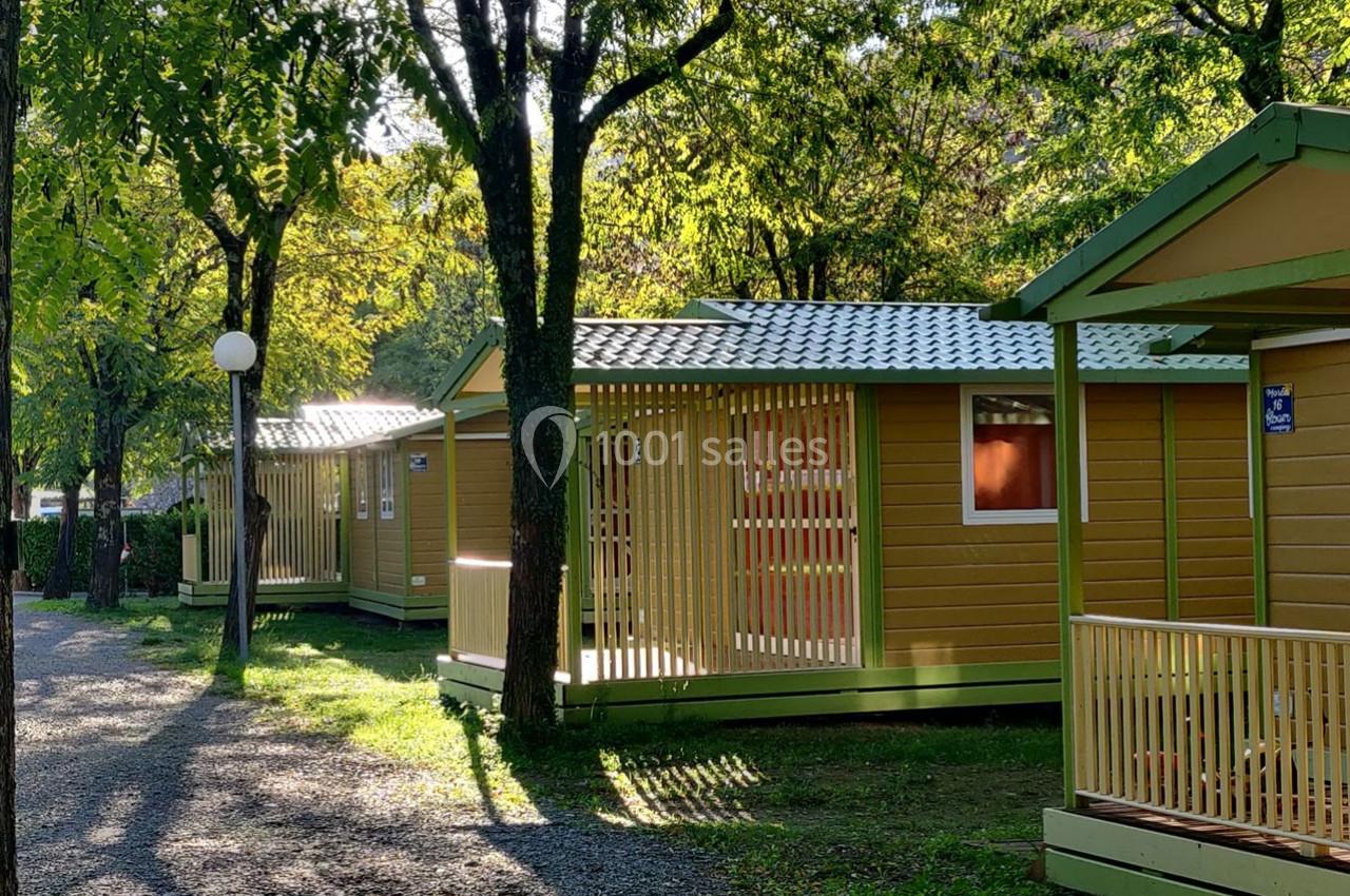 Alignement de chalets en bois jaunes avec terrasses, entourés d'arbres et éclairés par une lumière naturelle.