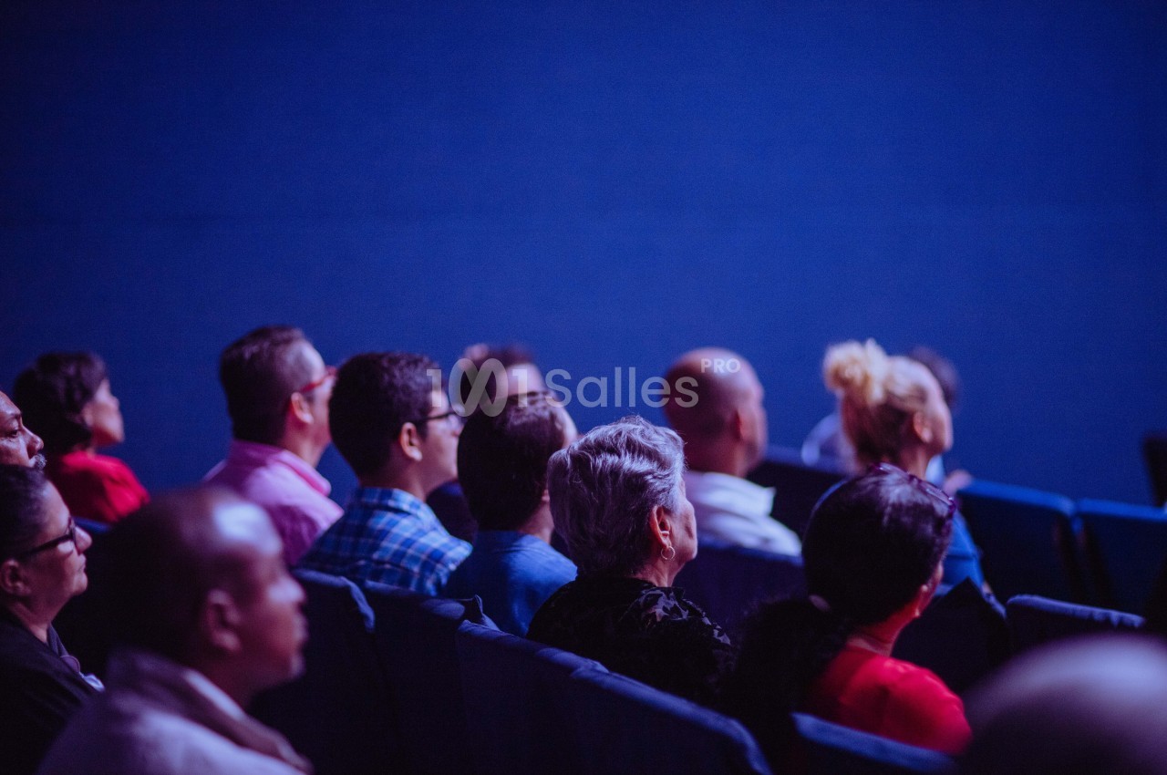 Des personnes assises dans une salle, regardant vers l'avant, dans une ambiance éclairée en bleu.