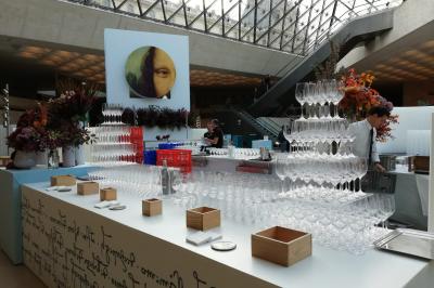 Salle de réception avec de longues tables dressées pour un événement, éclairée par des lumières chaudes.