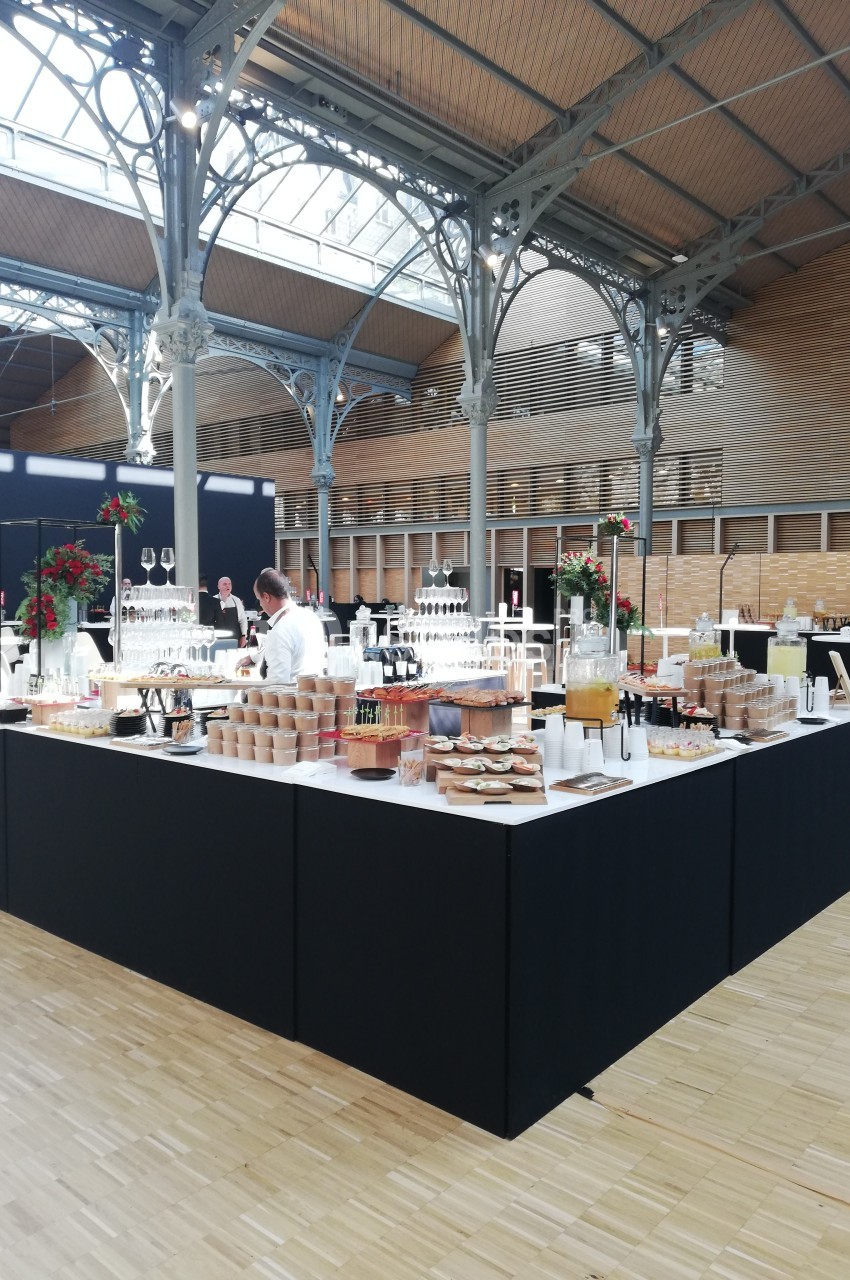 Buffet élégant avec boissons, viennoiseries et plats variés dans une grande salle lumineuse au style industriel.