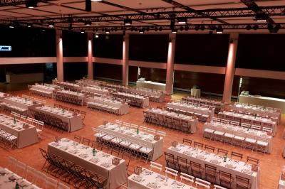 Salle de réception avec de longues tables dressées pour un événement, éclairée par des lumières chaudes.