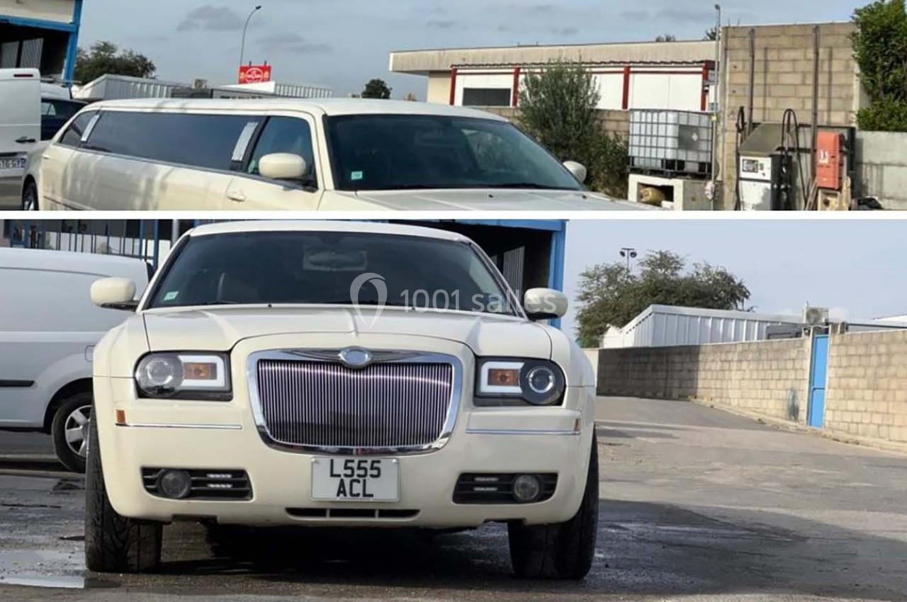 Voiture blanche de luxe, type limousine, stationnée devant un bâtiment industriel avec un parking en arrière-plan.