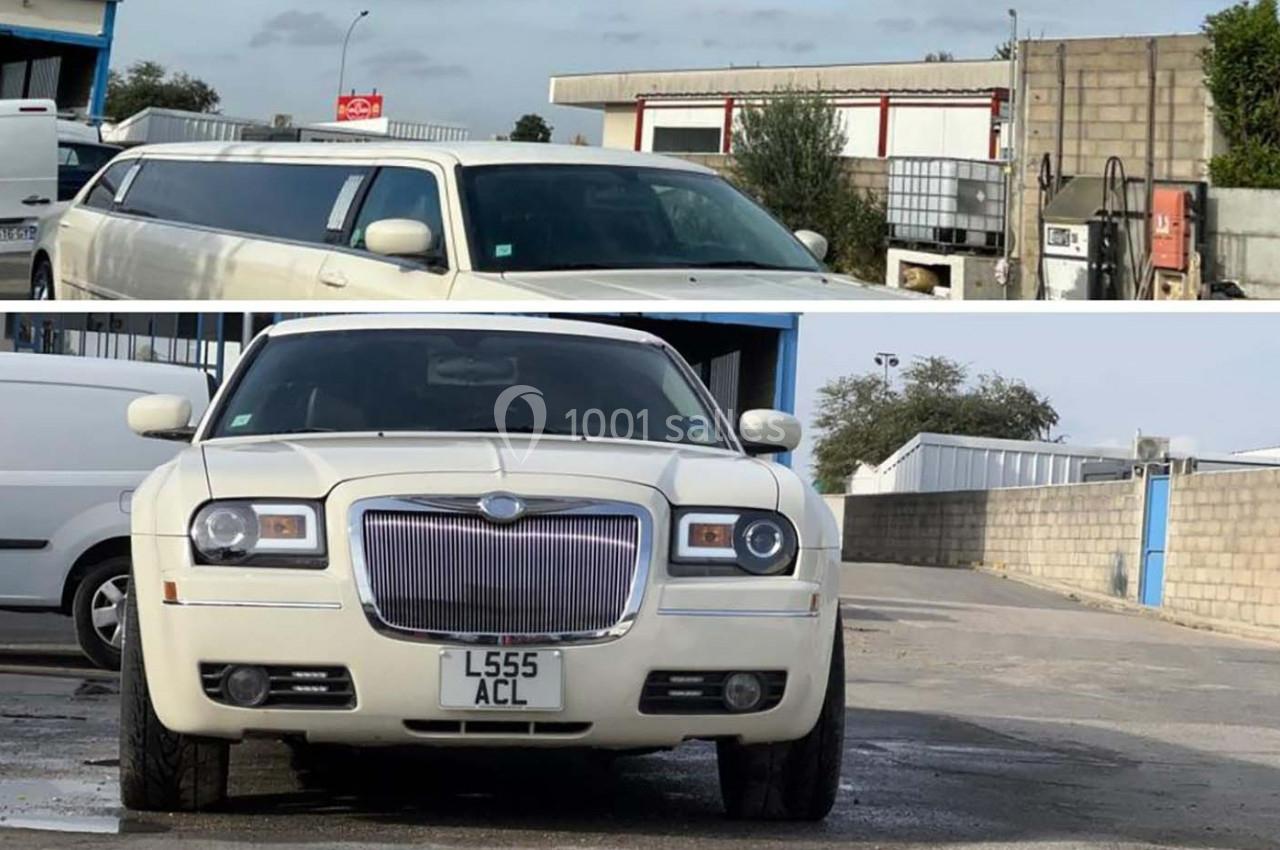 Voiture limousine blanche garée devant un bâtiment industriel avec un mur en parpaings en arrière-plan.