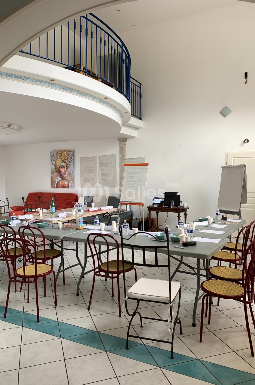 Salle lumineuse aménagée pour une réunion, avec une grande table entourée de chaises et des supports de présentation.