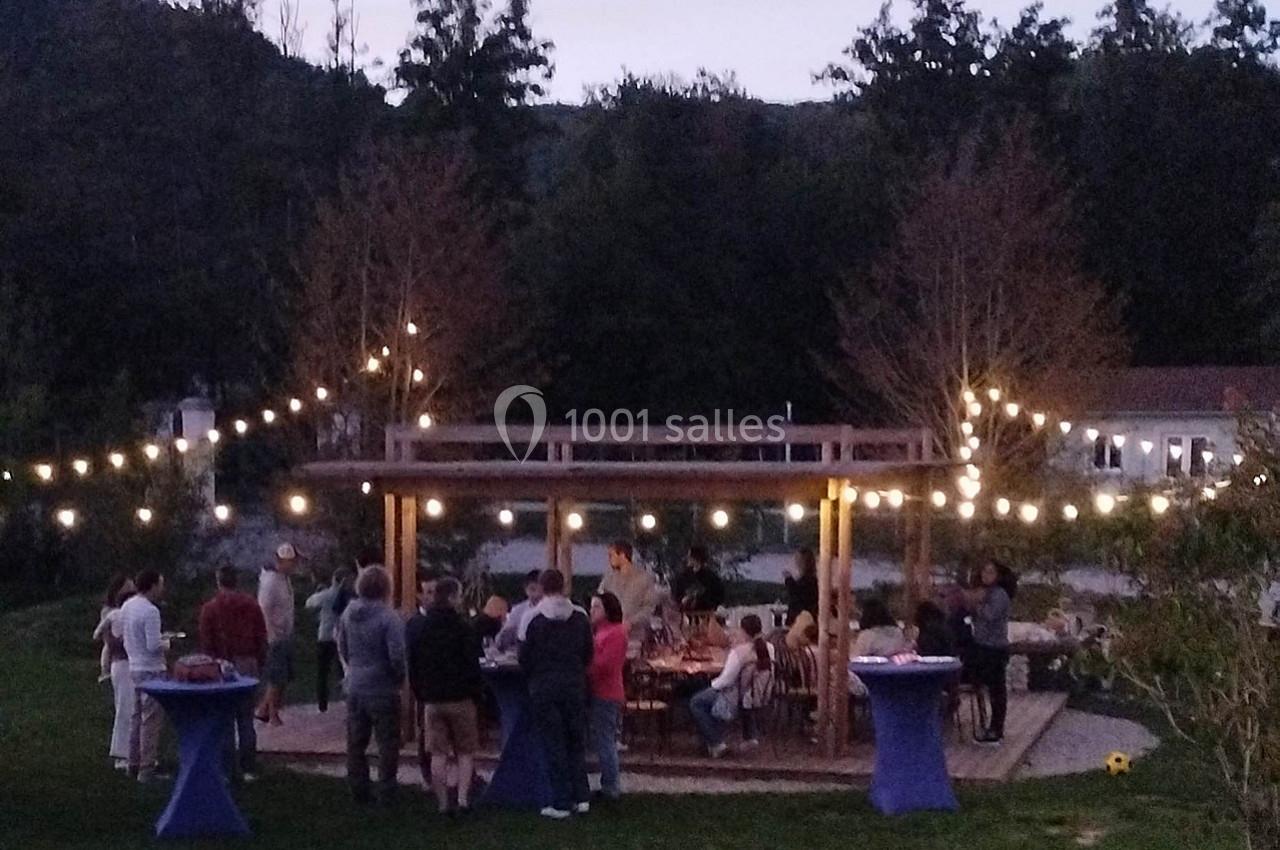 Groupe de personnes rassemblées sous une pergola éclairée par des guirlandes lumineuses dans un jardin au crépuscule.