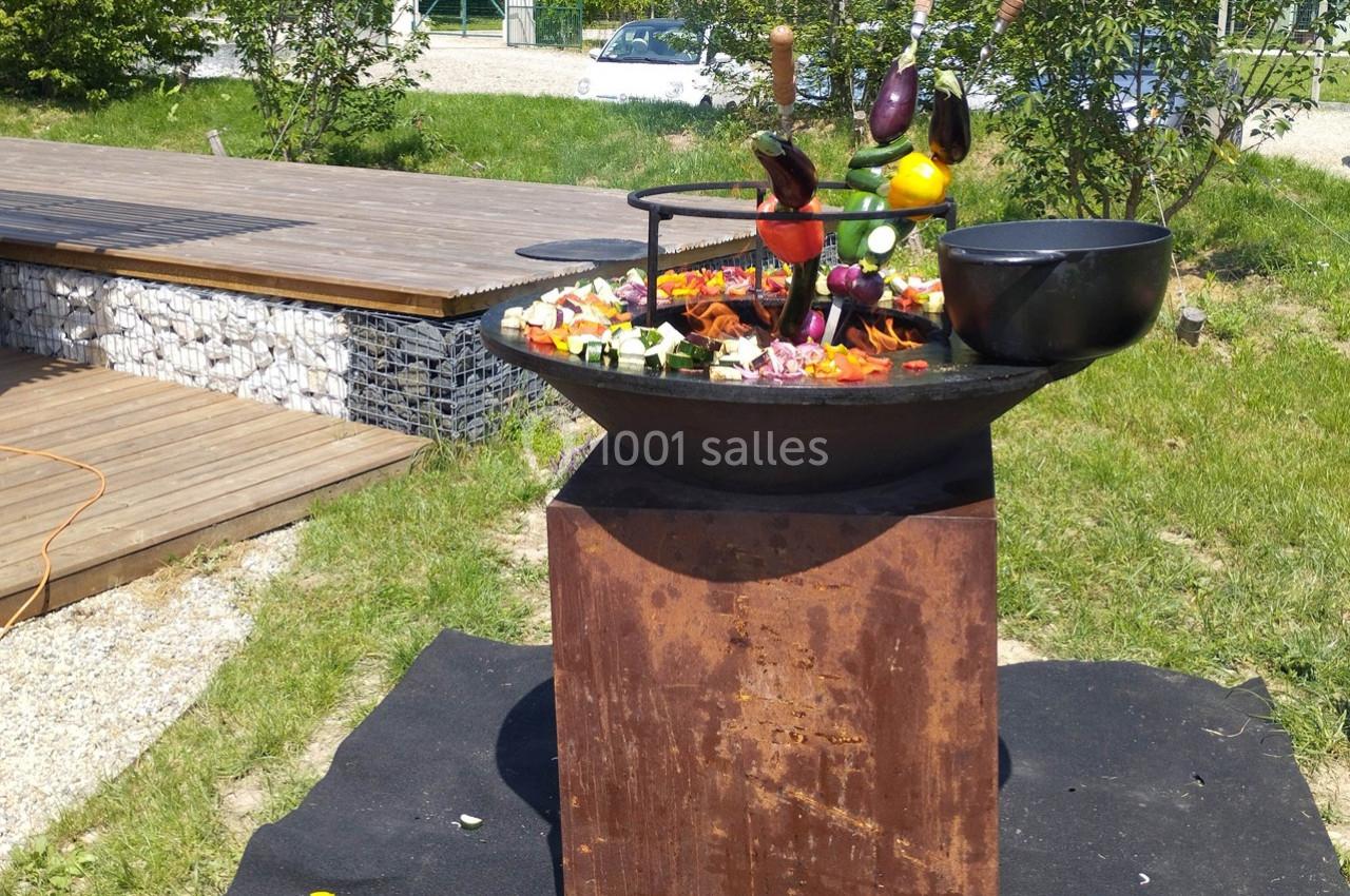 Légumes variés grillant sur une plancha en extérieur, entourée de verdure et d'une terrasse en bois.