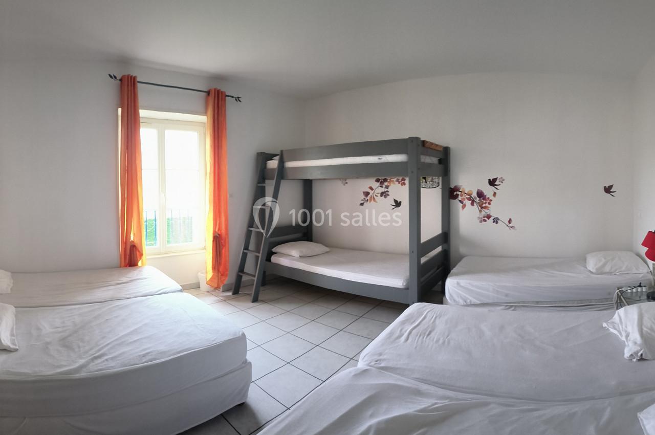 Chambre lumineuse avec lits simples, lits superposés, murs blancs, rideaux orange et décorations murales colorées.