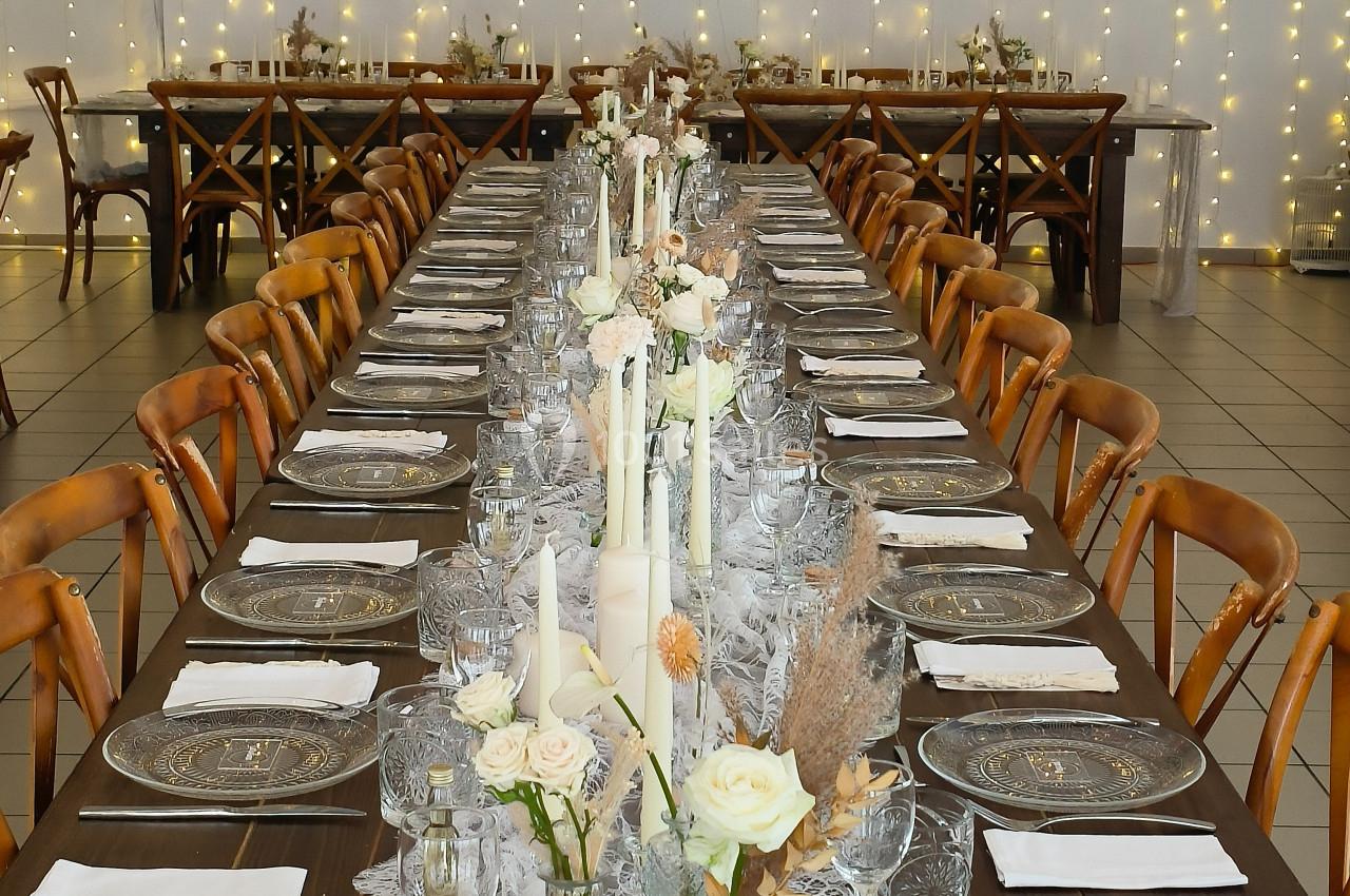 Grande table de réception décorée avec des bougies, des fleurs blanches et des guirlandes lumineuses en arrière-plan.