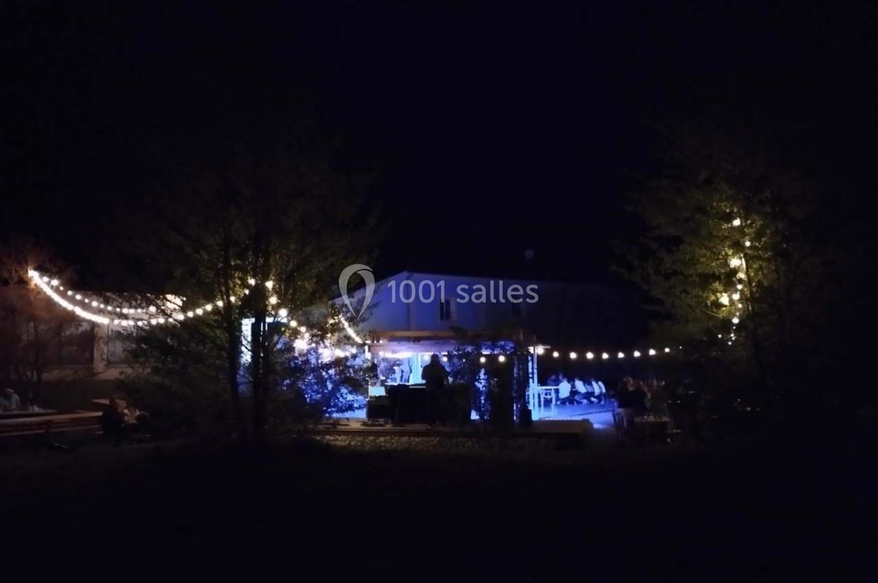 Maison illuminée la nuit avec des guirlandes lumineuses suspendues entre les arbres et autour d'une terrasse.