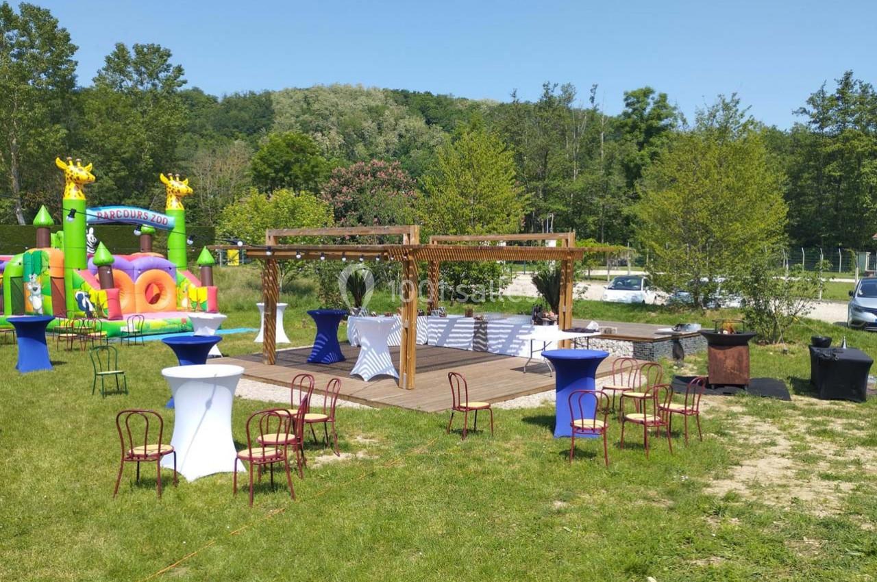 Espace extérieur aménagé avec pergola, tables hautes, chaises et structure gonflable colorée en arrière-plan.
