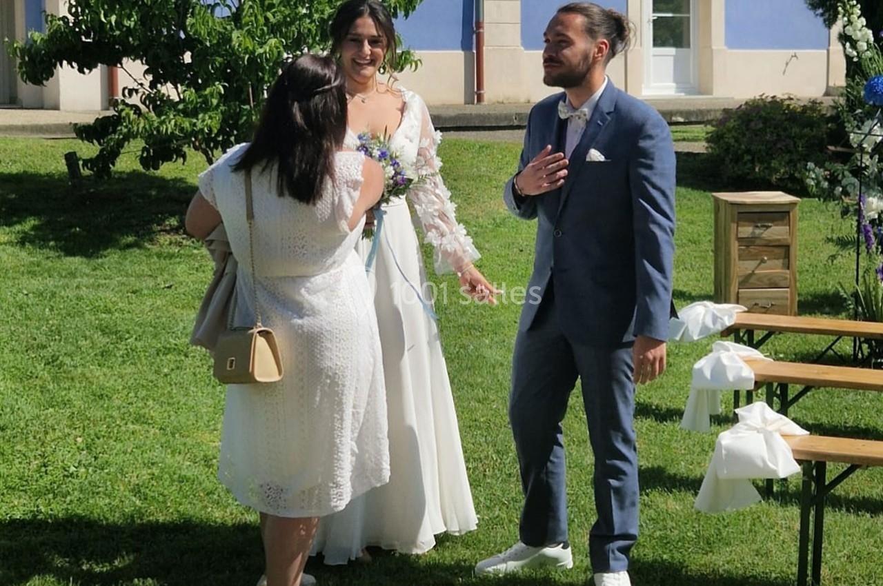 Une mariée et un marié discutent avec une invitée dans un jardin par une journée ensoleillée.