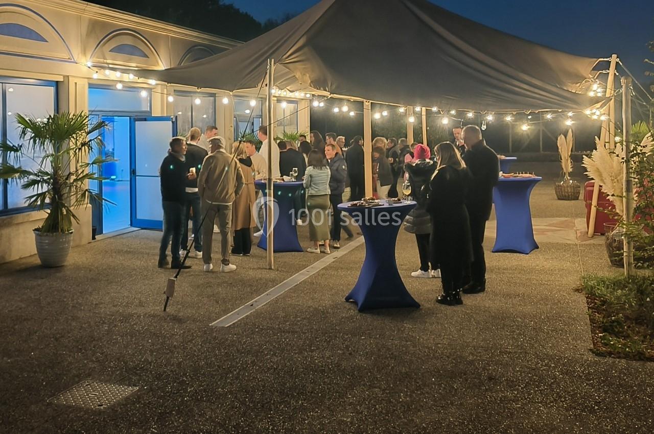 Groupe de personnes réunies sous une tente éclairée en soirée, avec des tables hautes et un décor extérieur.