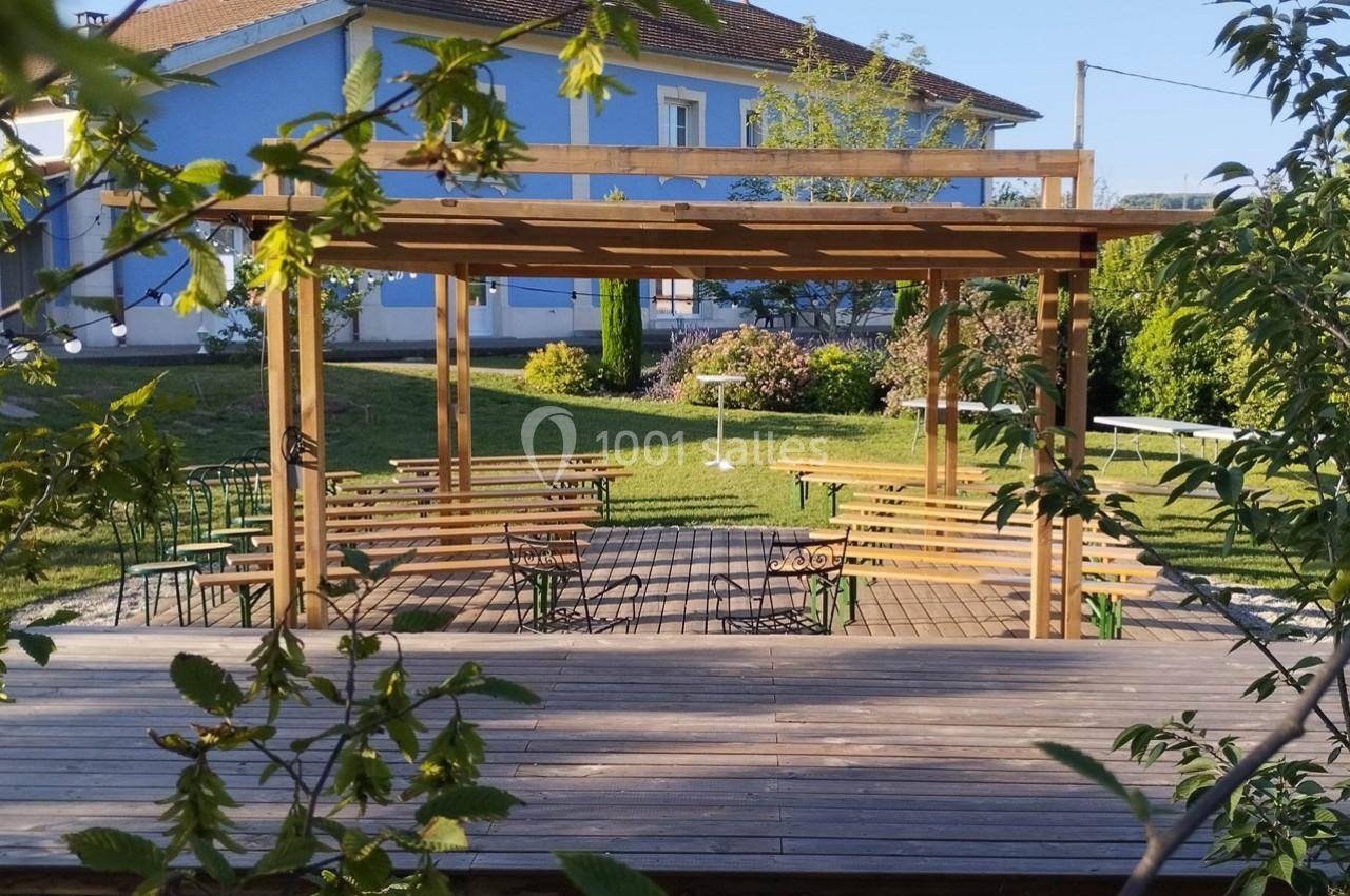 Pergola en bois sur une terrasse en bois, entourée de chaises et de verdure dans un jardin ensoleillé.