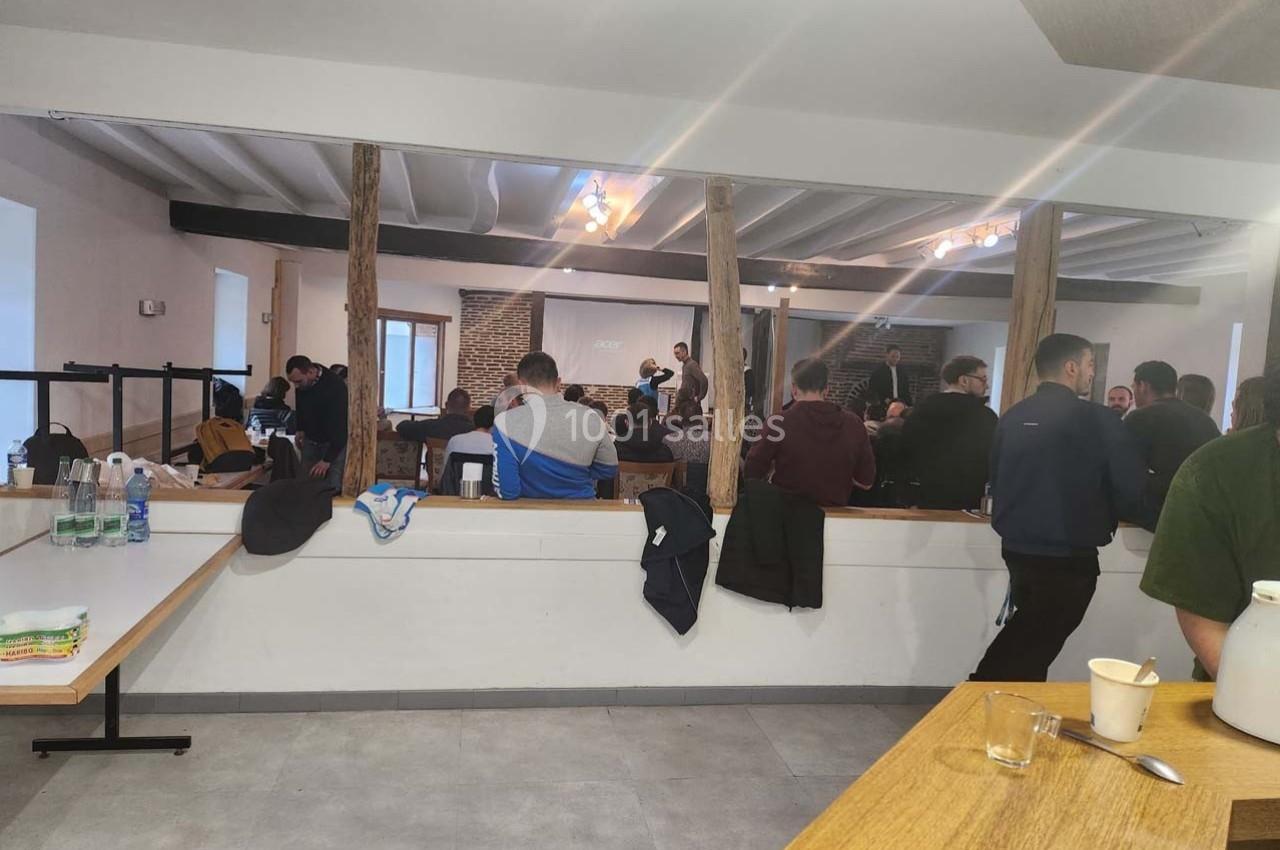 Un groupe de personnes assises et debout dans une salle avec des poutres apparentes, participant à une présentation.