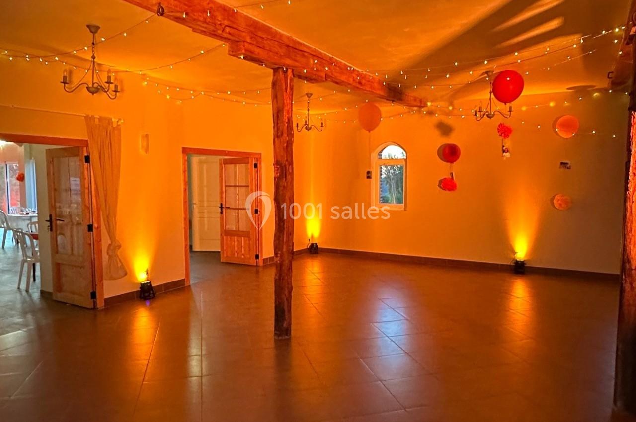 Salle spacieuse avec poutres en bois, éclairée par des guirlandes lumineuses et des lanternes suspendues.