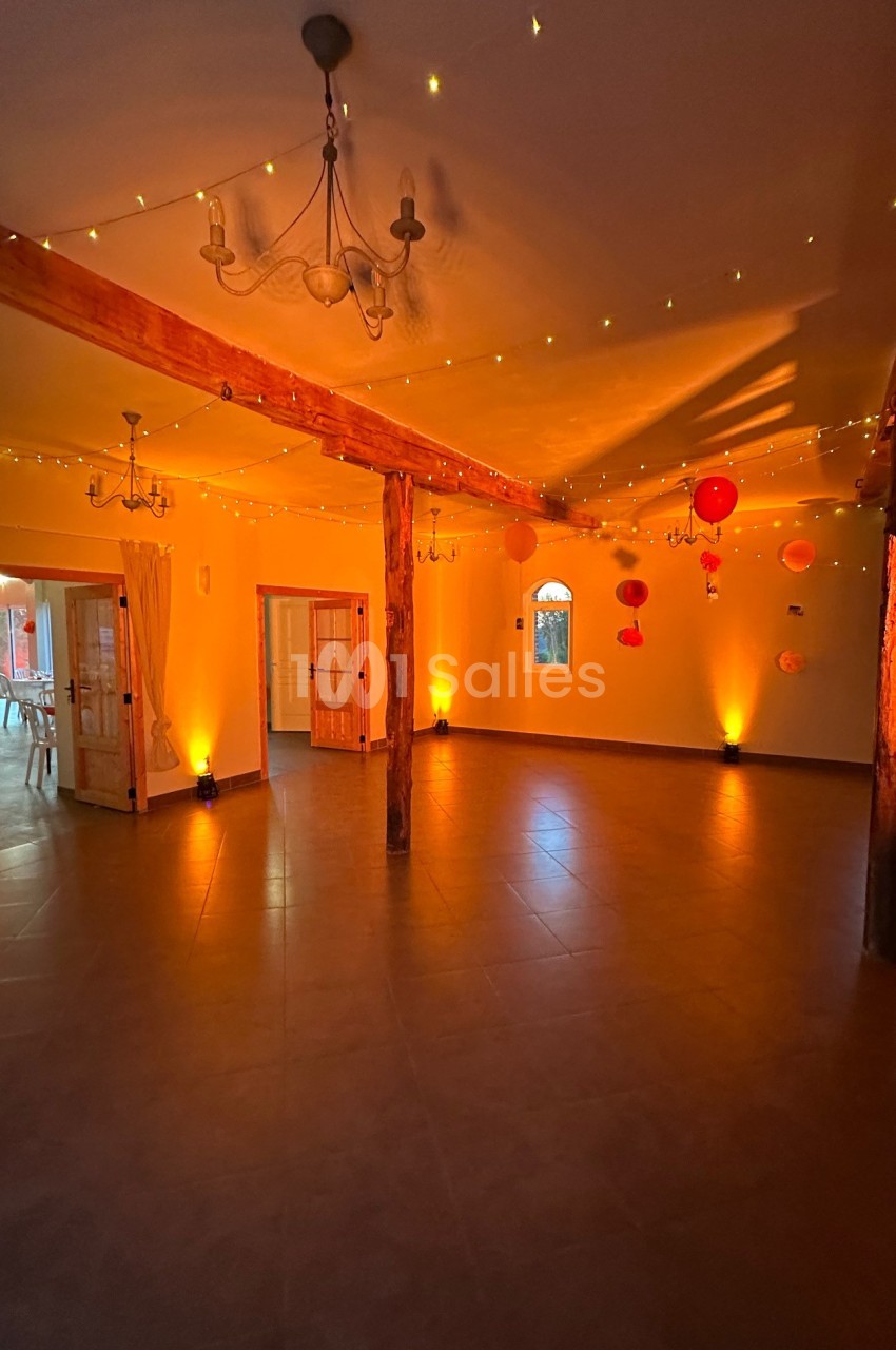Salle spacieuse avec poutres en bois, éclairée par des guirlandes lumineuses et des lanternes suspendues.