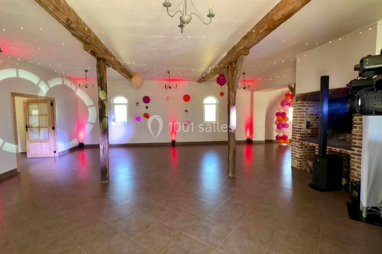 Salle spacieuse décorée de guirlandes lumineuses, ballons colorés et éclairages rouges, avec poutres apparentes.