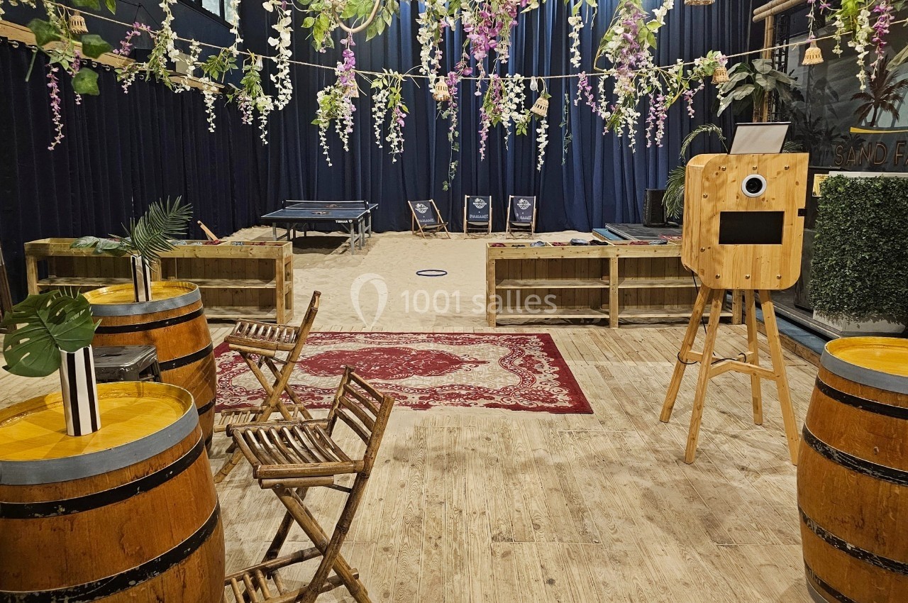 Espace intérieur décoré avec des tables en tonneaux, chaises en bois, tapis rouge et guirlandes suspendues.