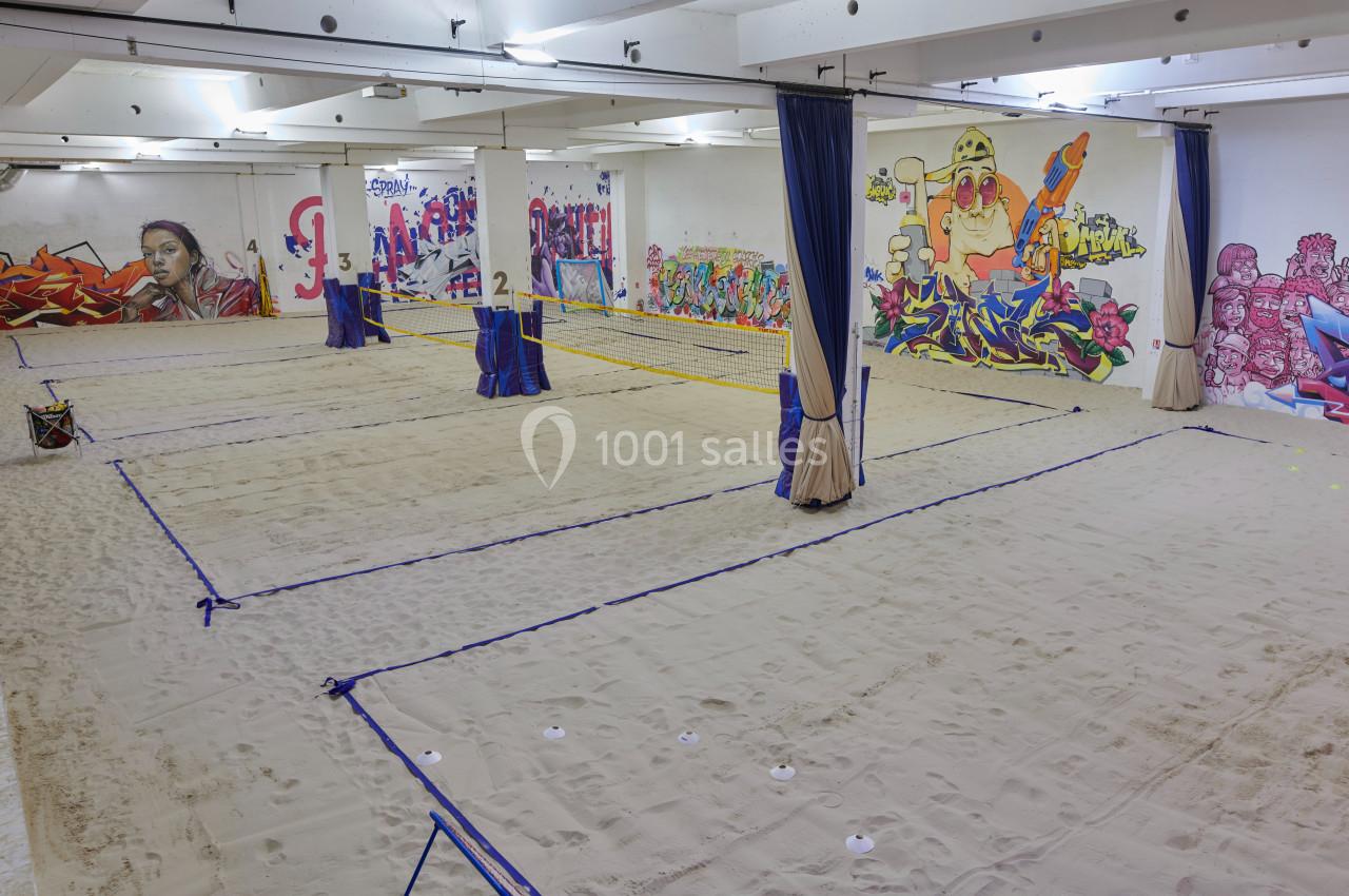 Terrain de beach-volley intérieur avec sol en sable, filets tendus et murs décorés de graffitis colorés.