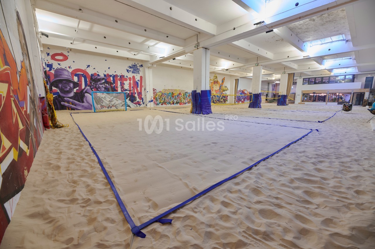 Terrain de sable intérieur délimité par des lignes bleues, entouré de murs décorés de graffitis colorés.