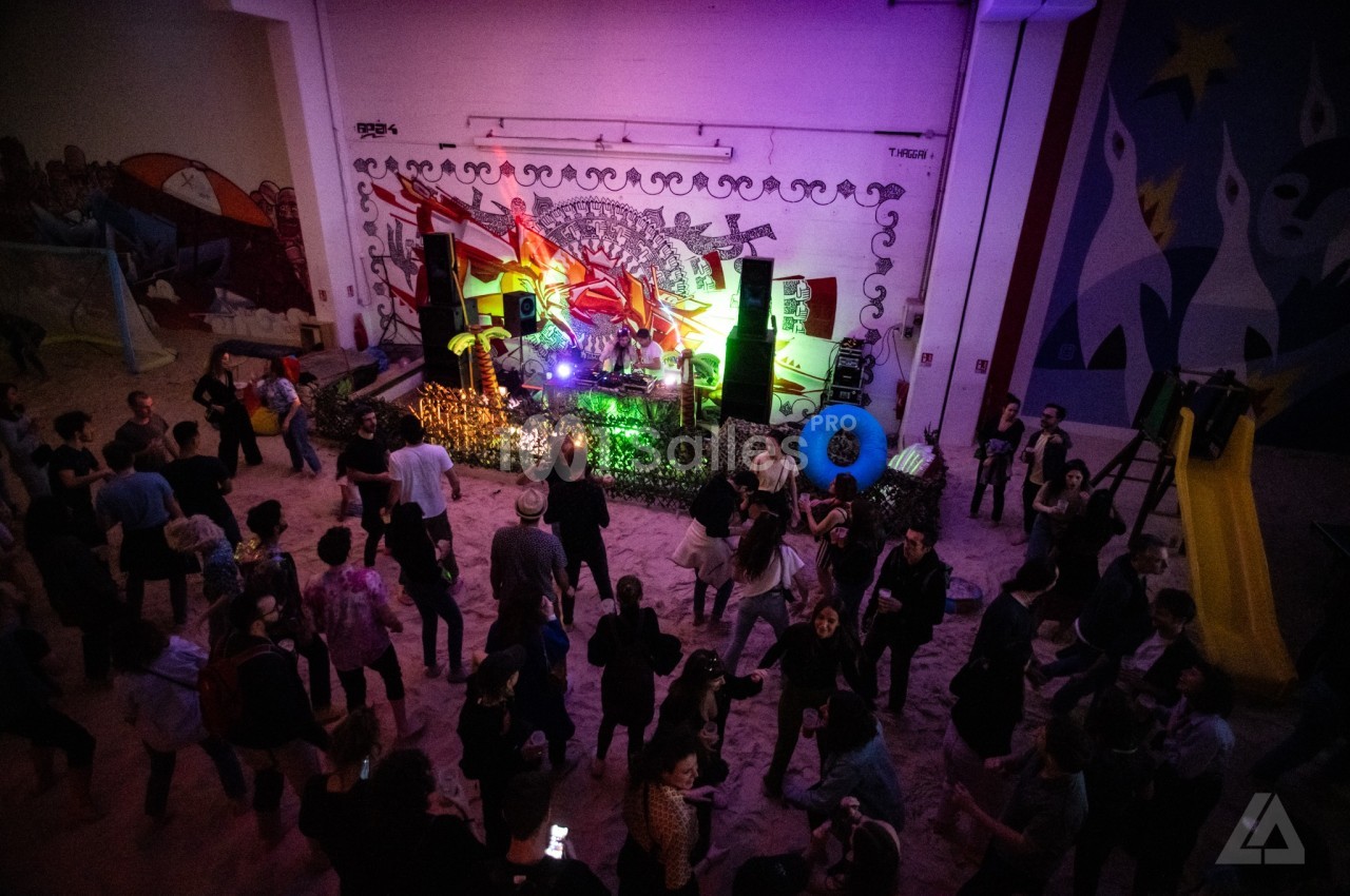 Groupe de personnes dans une salle colorée avec un DJ sur une scène décorée et des graffitis en arrière-plan.