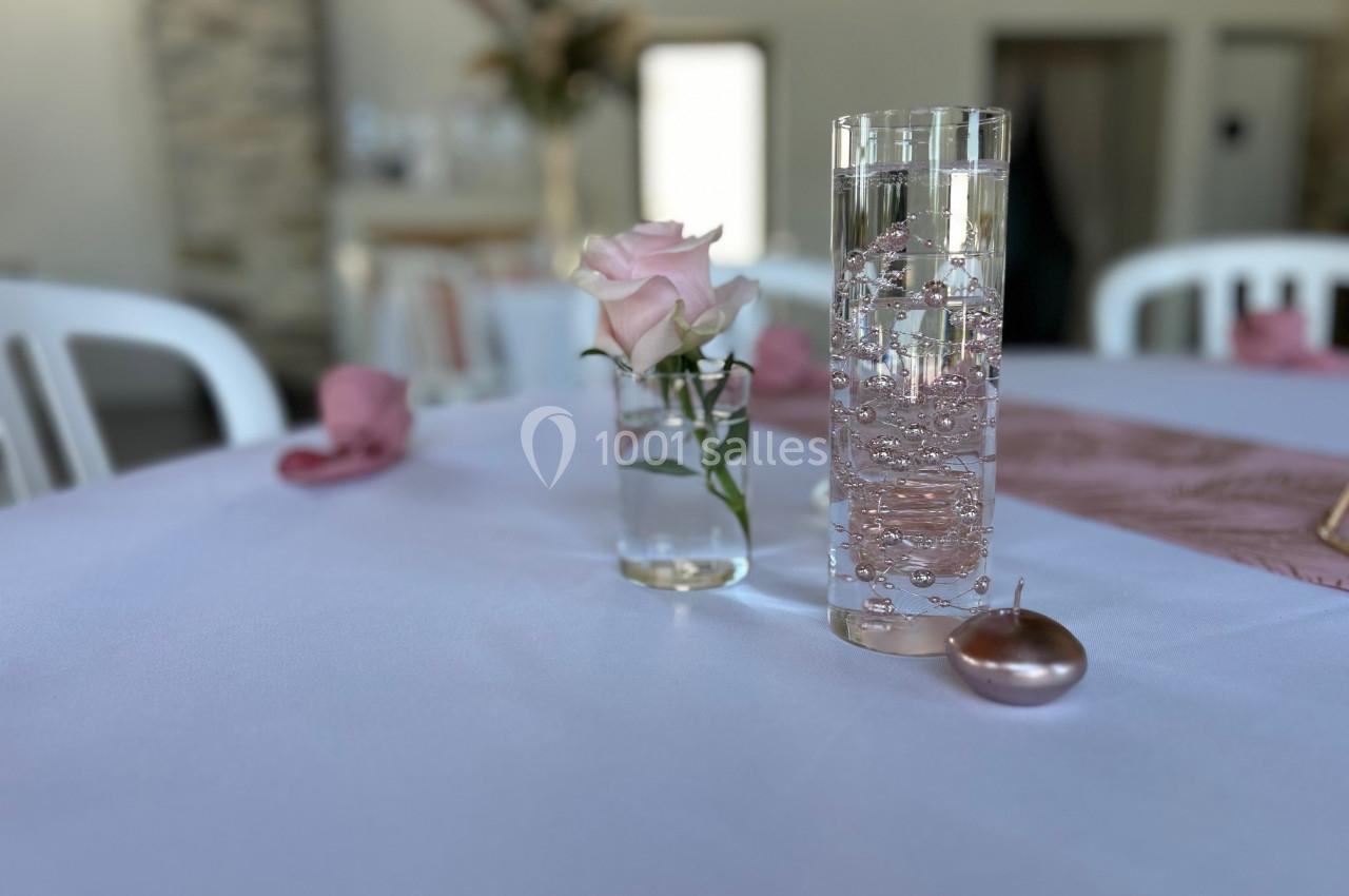 Vase avec une rose rose et verre d'eau pétillant sur une table blanche décorée de serviettes roses.