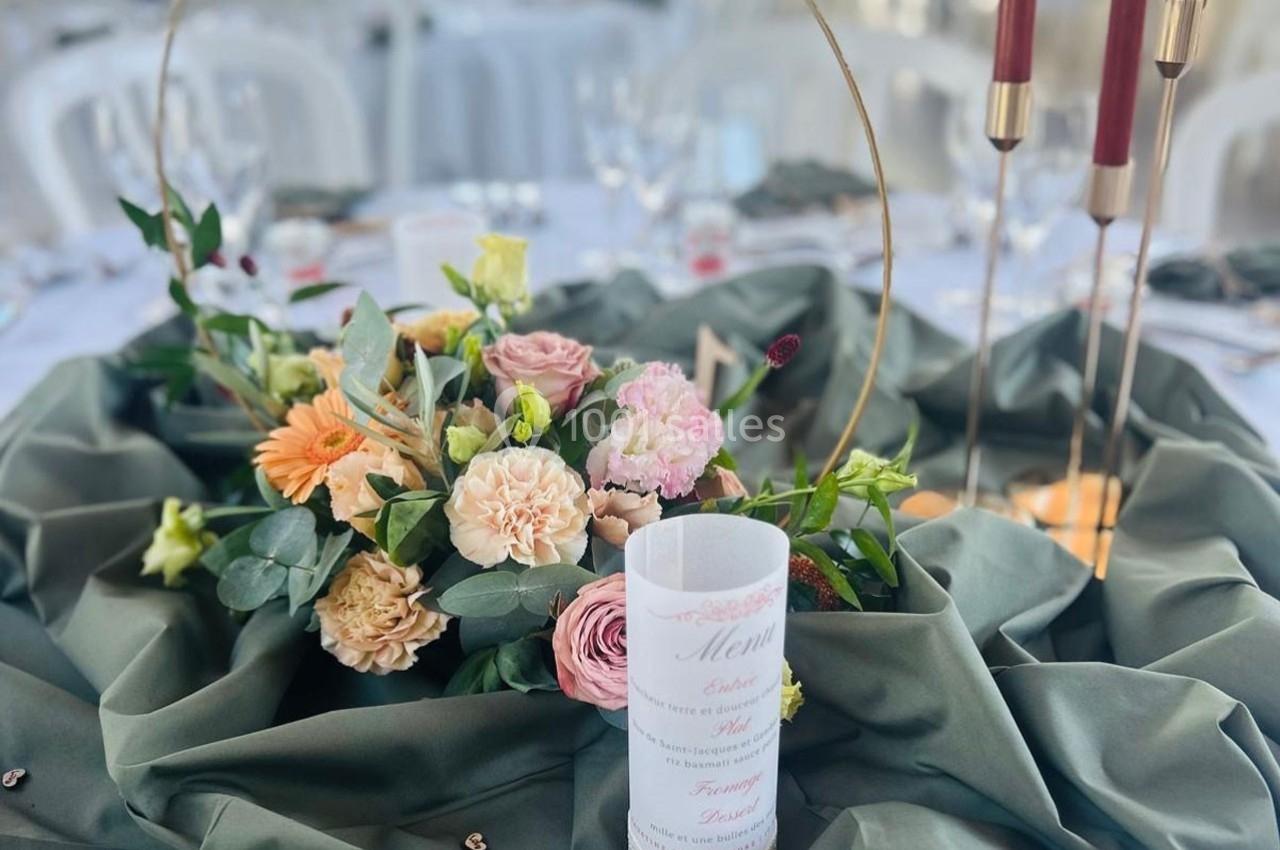 Centre de table avec fleurs colorées, bougies rouges et menu placé sur une nappe verte élégamment drapée.